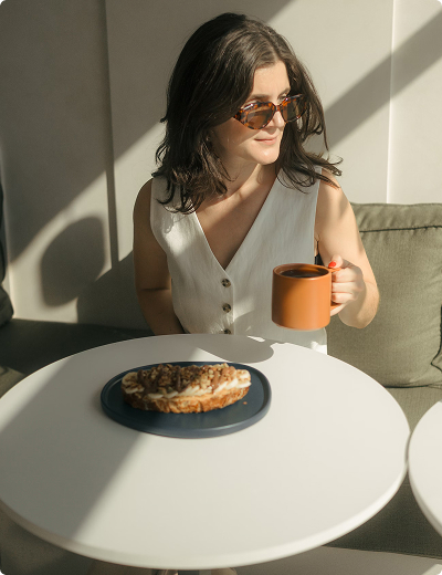 Woman drinking a mug of coffee with a plate of cake on a table in front of her