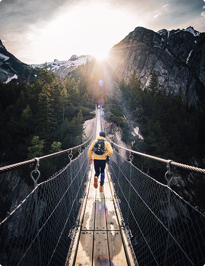 man jogging over a hanging bridge in a mountain setting wearing a backpack on his own