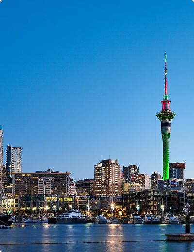 <span>Virtual cards</span> for online and in-store use Auckland city skyline at dusk in New Zealand, with the Sky Tower lit in red and green, buildings aglow, and boats docked in the foreground.