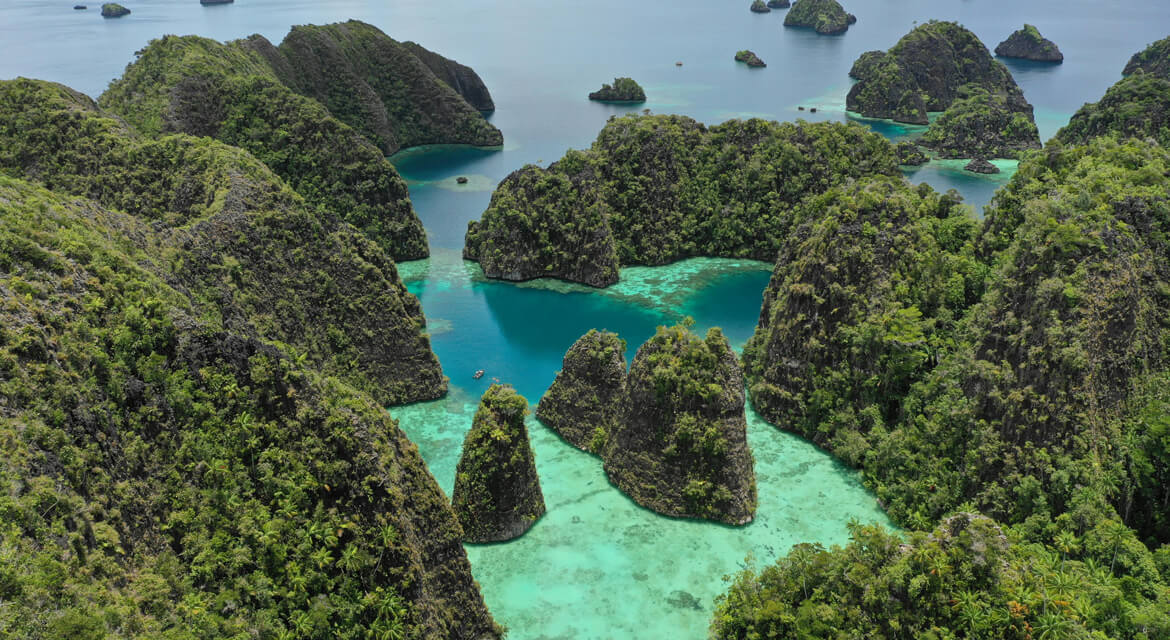 Aerial view of lush green islands scattered across turquoise and deep blue waters in a tropical archipelago.