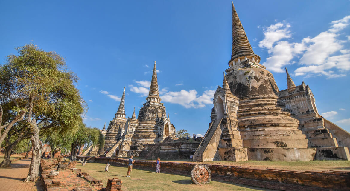 Historic site in Ayutthaya featuring large weathered stupas surrounded by grassy grounds and scattered bricks under a clear sky, capturing Thailand’s rich heritage and archaeological significance