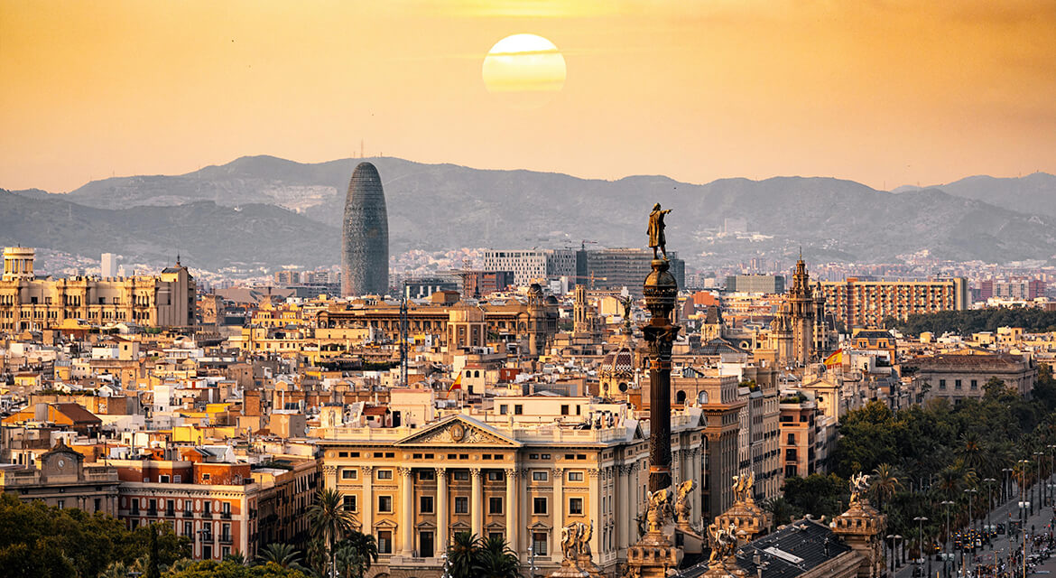 Sunset view of Barcelona with the Columbus Monument, historic buildings, and Torre Glòries in the skyline, capturing the city’s blend of Gaudí architecture, Mediterranean charm, and travel-ready atmosphere
