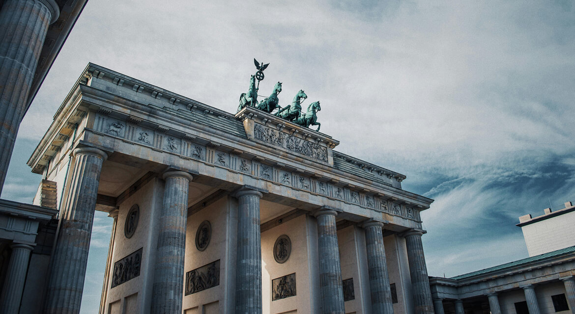 View of the Brandenburg Gate in Berlin with its neoclassical columns and Quadriga sculpture under a partly cloudy sky, symbolizing Germany’s unity and cultural richness amid a vibrant urban backdrop