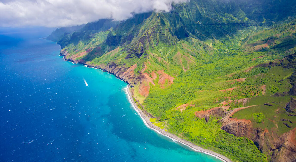 Aerial view of lush green cliffs and turquoise waters along Hawaii’s Nā Pali Coast, capturing the state’s dramatic landscapes and relaxed tropical vibe.