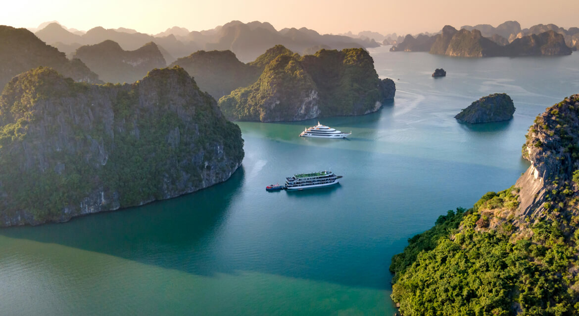 Aerial view of Halong Bay with emerald green waters and lush limestone islands featuring cruise ships and boats, capturing the natural beauty and adventure appeal of this iconic Vietnamese destination