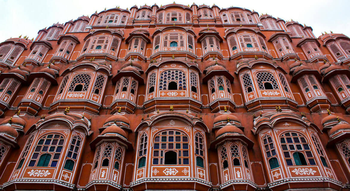The facade of Hawa Mahal in Jaipur with its red and pink sandstone lattice windows and tiered architecture reflecting traditional Rajput design