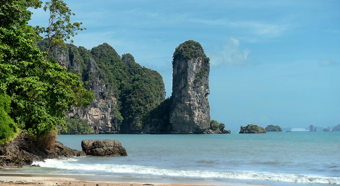 Scenic coastal view in Krabi with towering limestone karst formations, turquoise waters, sandy beach, and tropical foliage, showcasing the region’s dramatic natural beauty and appeal to nature lovers