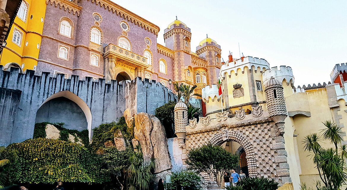 View of Pena Palace in Sintra near Lisbon with vivid yellow, red, and purple towers surrounded by greenery and rocky cliffs, showcasing Portugal’s romantic architecture and scenic coastal allure
