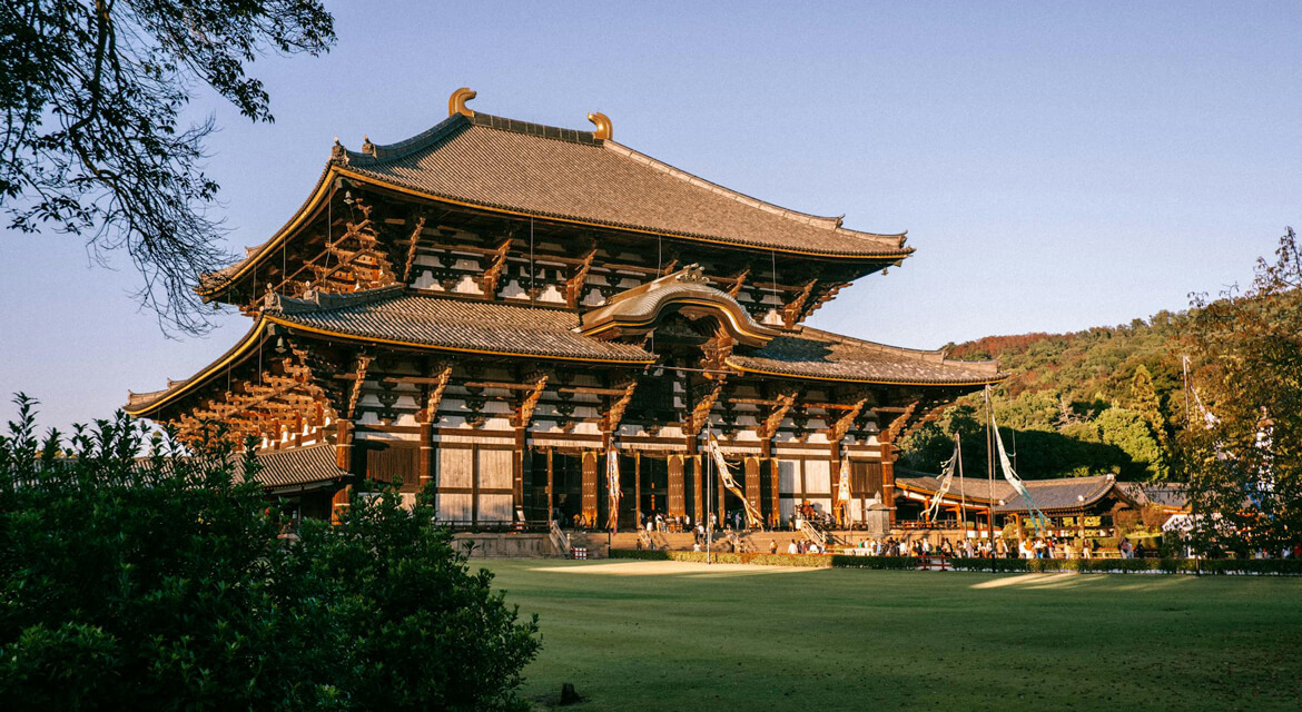 View of Todai-ji Temple in Nara with traditional wooden architecture surrounded by greenery and visitors, highlighting the city's historical significance and tranquil atmosphere