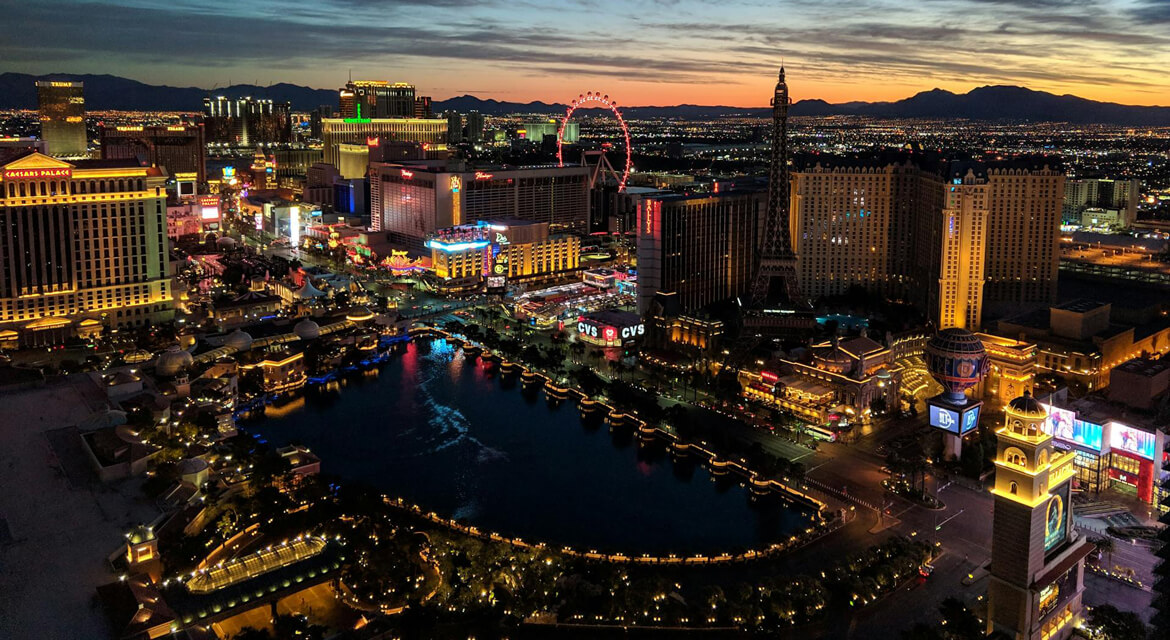 A dazzling aerial view of the Las Vegas Strip at night, featuring iconic landmarks like the Bellagio fountains and Eiffel Tower replica, capturing the city’s vibrant entertainment, luxury, and proximity to natural wonders like the Grand Canyon.
