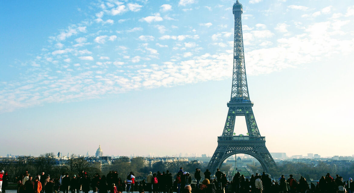 View of the Eiffel Tower with crowds gathered on a plaza under a clear sky, capturing Paris’s blend of iconic landmarks, walkable streets, and cultural allure