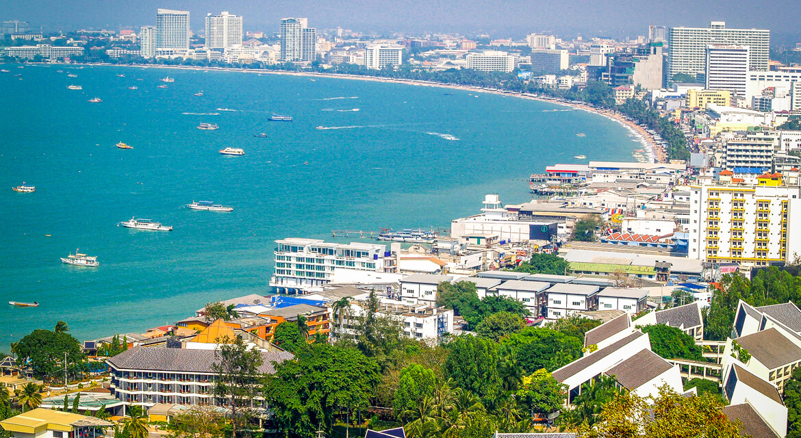 Aerial view of Pattaya’s coastline with curved sandy beach, turquoise waters filled with boats, and high-rise buildings lining the shore, showcasing the city’s lively atmosphere and recreational appeal
