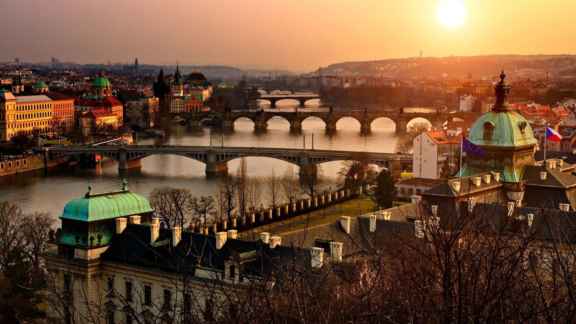 Sunset view of Prague with historic bridges over the Vltava River, including Charles Bridge, and classic domed architecture, capturing the city’s romantic atmosphere and European heritage