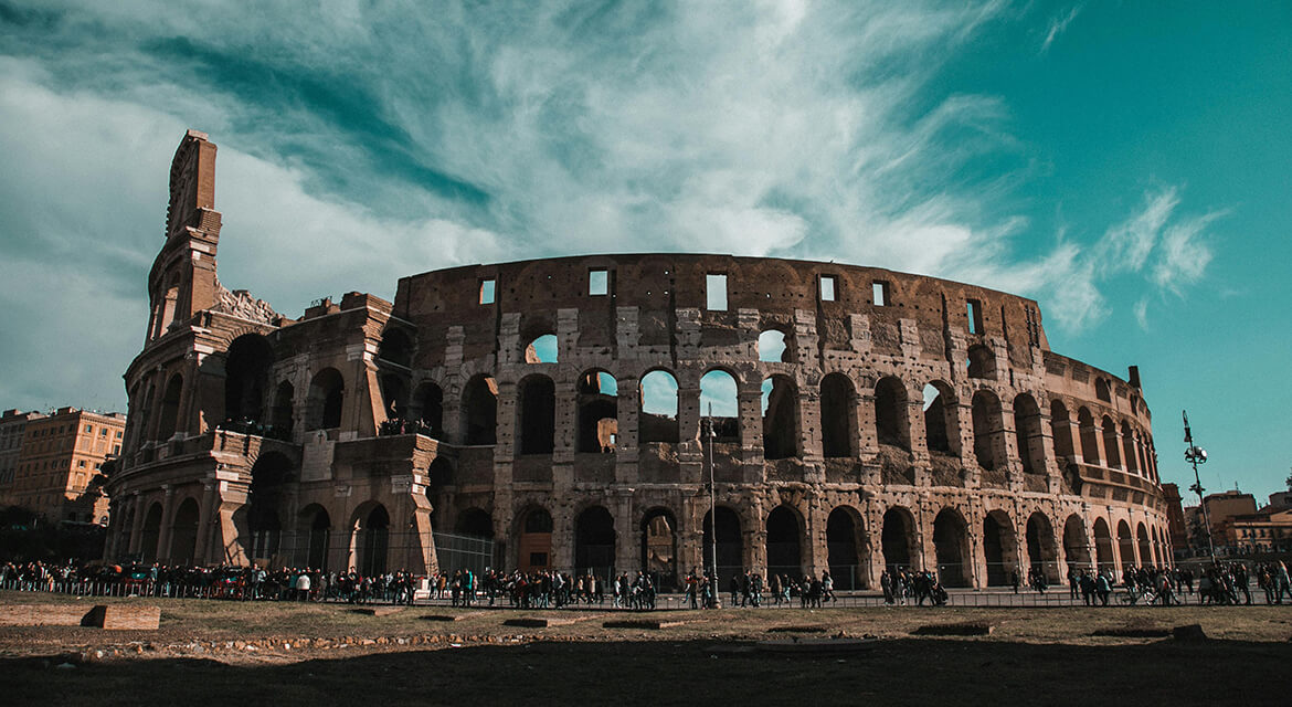 View of the Colosseum in Rome with crowds gathered under a partly cloudy sky, showcasing Italy’s historic architecture and the ease of exploring the city with Euro currency