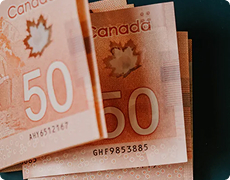 Stacked Canadian fifty dollar banknotes with maple leaf design Several Canadian $50 bills stacked together showing red color, maple leaf symbol, and visible serial numbers representing Canadian currency