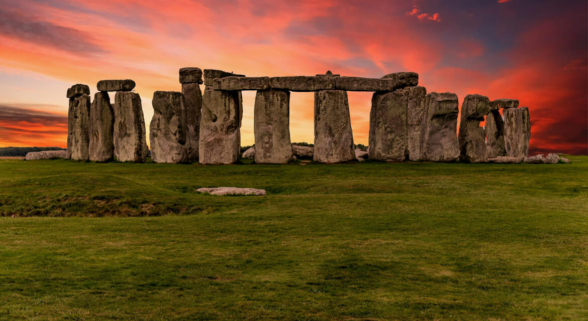 Dramatic sunset view of Stonehenge with towering prehistoric stones silhouetted against vibrant red and orange sky in Wiltshire England
