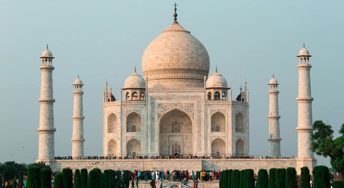 The Taj Mahal in Agra with its white marble dome and four minarets surrounded by gardens and visitors under a soft sky