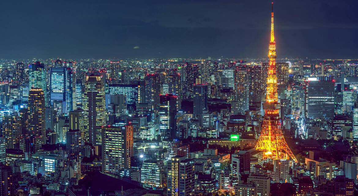 Nighttime view of Tokyo featuring the illuminated Tokyo Tower surrounded by high-rise buildings, showcasing the city's blend of modern architecture and traditional charm