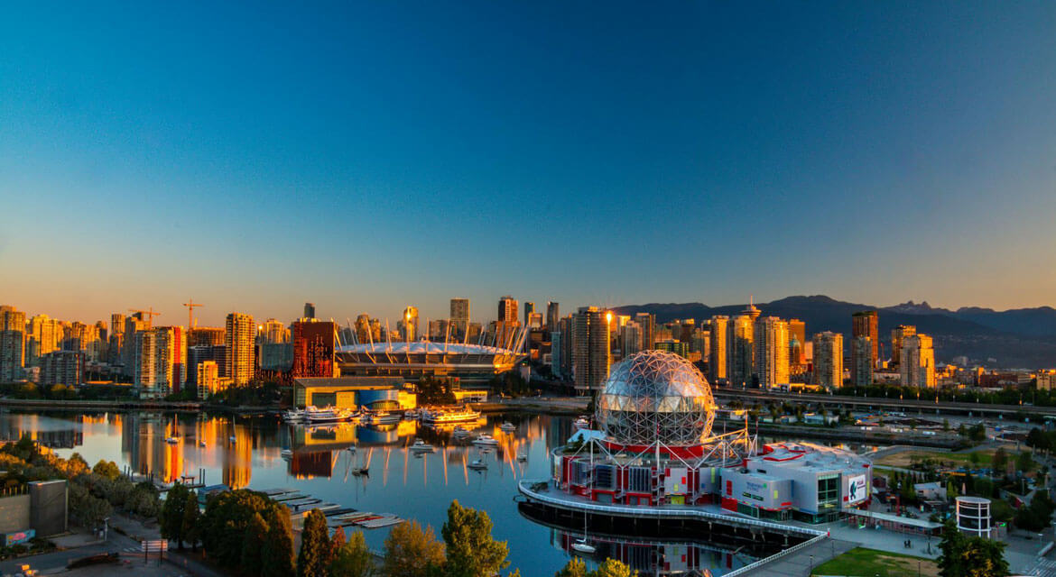 View of Vancouver’s waterfront at sunset with Science World’s geodesic dome, BC Place Stadium, modern buildings, and mountains reflecting in False Creek